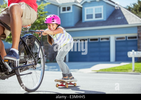 Padre sulla bicicletta la figlia di tiro su skateboard Foto Stock