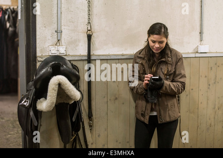 Giovane donna utilizzando smart phone a cavallo stabile Foto Stock