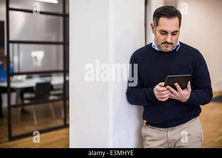 Adulto medio imprenditore utilizzando digitale compressa mentre appoggiato su colonna in ufficio Foto Stock