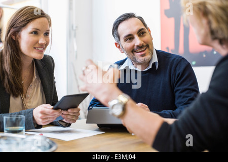 Imprenditori sorridente con digital compresse discutendo alla scrivania in ufficio Foto Stock