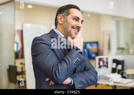 Sorridente adulto medio imprenditore con mano sul mento che guarda lontano in office Foto Stock