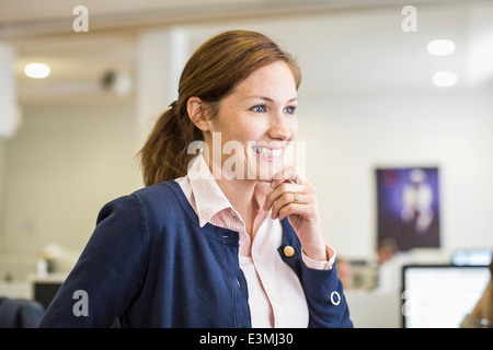 Imprenditrice sorridente con la mano sul mento che guarda lontano in office Foto Stock