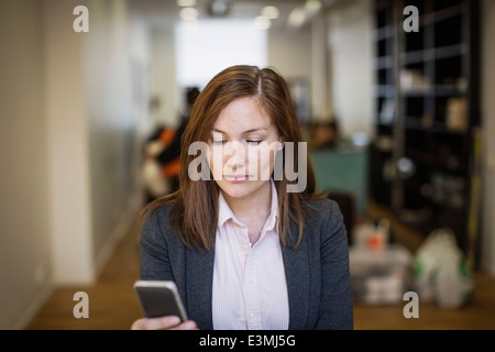 Imprenditrice tramite cellulare in ufficio Foto Stock