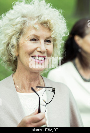 Felice senior donna che guarda lontano mentre si tiene gli occhiali in posizione di parcheggio Foto Stock