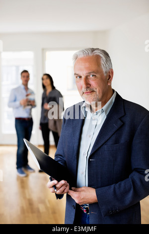 Ritratto del maschio fiducioso agente immobiliare con coppia in piedi in background a home Foto Stock