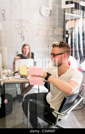 Giovane imprenditore iscritto idee su note adesive con il collega in background al nuovo ufficio Foto Stock