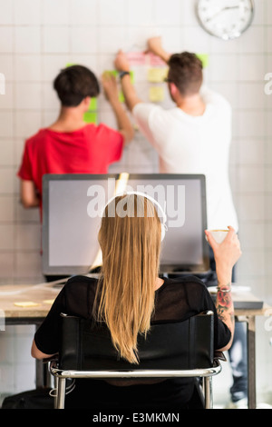 Vista posteriore del giovane imprenditrice avente il caffè con i colleghi di sesso maschile in background in ufficio creativo Foto Stock