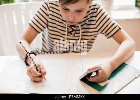 Angolo di alta vista di boy utilizzando il telefono cellulare mentre studiava a tavola in casa Foto Stock