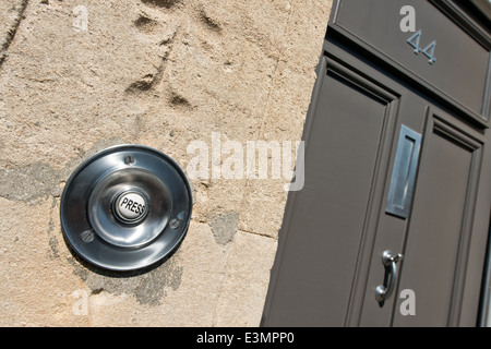 Una circolare cromato campanello della porta su un bagno a spiovente muro di pietra con la parola premere sul pulsante con una porta anteriore Foto Stock