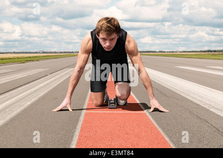 Atleta maschio sulla pista di aeroporto preparando per il suo inizio Foto Stock