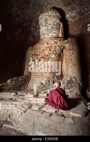 Giovane monaco seduto di fronte a un vecchio statua del Buddha, Bagan, Myanmar, Asia. Foto Stock