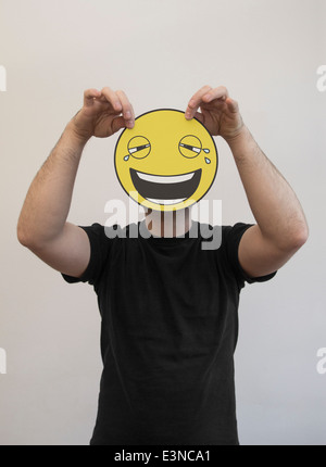 L'uomo tenendo un ridere e piangere emoticon nella faccia anteriore del suo volto Foto Stock