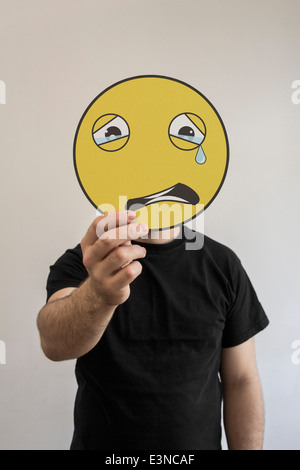 L'uomo tenendo un pianto emoticon nella faccia anteriore del suo volto Foto Stock