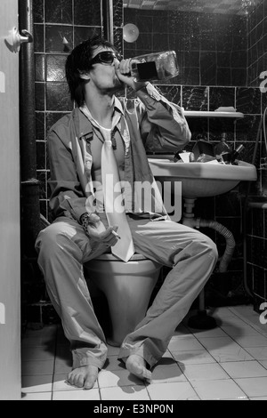 Uomo ubriaco si siede in una toilette bere whisky e fumatori, immagine in scala di grigi Foto Stock