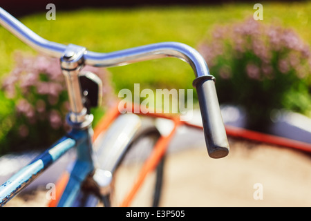 Vintage manubrio di bicicletta dettaglio chiudere con parcheggio sfondo bokeh di fondo nel letto di fiori in giornata soleggiata Foto Stock