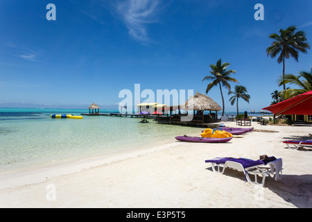 Rilassante paesaggio di un resort sulla spiaggia con sabbia bianca, capanne tikki con tetto di paglia e palme. Foto Stock