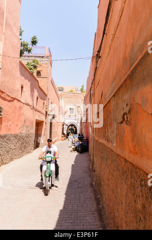 Un uomo che cavalca un scooter lungo una strada stretta nella città vecchia di Marrakech, Marocco Foto Stock