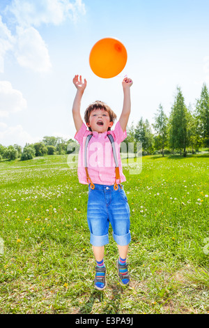 Ragazzo carino con palloncino arancione nel campo verde Foto Stock