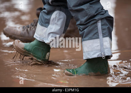Stivali in gomma sono visti a piedi attraverso i campi fangosi di azienda agricola degna durante il 2014 Festival di Glastonbury nel Somerset, Giugno 2014. Foto Stock