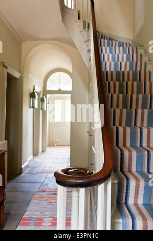 Striped Christine van der Hurd runner su scala con ringhiera in legno in lastricato hall di entrata Foto Stock