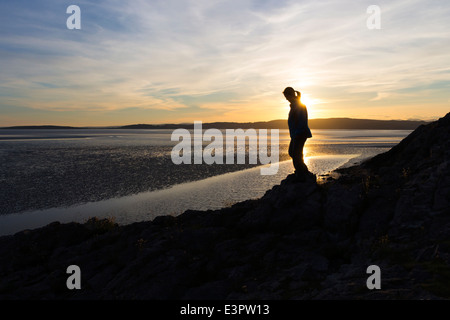 Donna che cammina lungo la costa Silverdale al tramonto, Morecambe Bay, Lancashire, Inghilterra, Regno Unito Foto Stock