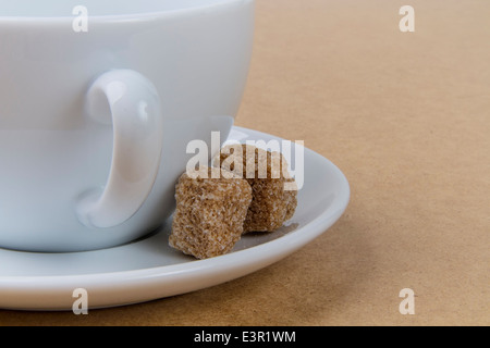 Rough cut zucchero di canna a cubetti con un bianco tazza da caffè con piattino Foto Stock