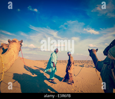 Vintage retrò hipster stile immagine di viaggio del Rajasthan travel background - due indiani cameleers (camel driver) con i cammelli Foto Stock