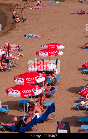 La gente a prendere il sole su di una spiaggia di sabbia sulle sedie a sdraio sotto gli ombrelloni Foto Stock