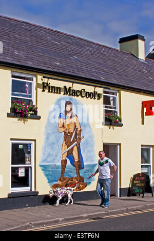 Uomo e cane a piedi passato murale di Finn MacCool su Finn MacCool's pub in Bushmills, Co. Antrim, Ulster (Irlanda del Nord Foto Stock