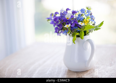 Bouquet di fiori selvatici in bianco vaso sulla tavola in legno rustico vicino a finestra con copia spazio, luce naturale Foto Stock