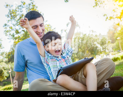 Bella gara di misto di padre e figlio la riproduzione su un computer Tablet all'esterno. Foto Stock