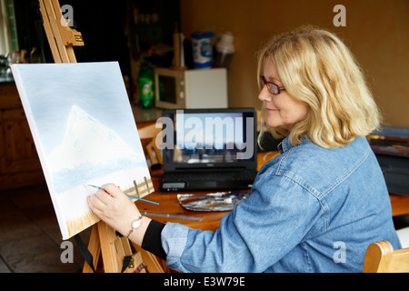 Donna pittura in cucina con fotografia sullo schermo del computer come riferimento Foto Stock