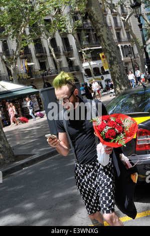 Ragazzo moderno con fiori in attesa di un taxi e di controllare il suo cellulare a Las ramblas di Barcellona Foto Stock