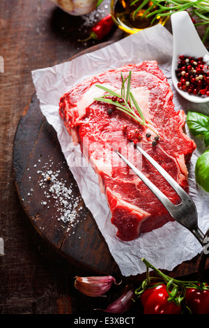 Materie bistecca con forcella di carne e gli ingredienti su sfondo di legno Foto Stock