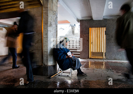 Un mendicante donna seduta in un giorno di pioggia in un passaggio sotterraneo Foto Stock