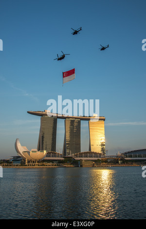 Elicotteri volare la bandiera di Singapore al tramonto sulla baia di Marina durante le prove della celebrazione della festa nazionale Foto Stock