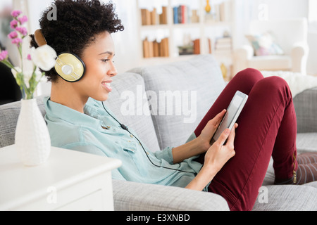 Nero donna in ascolto delle cuffie sul divano Foto Stock