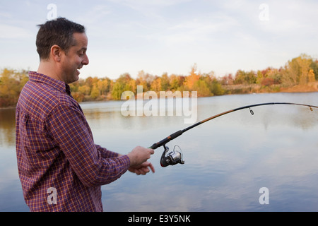 Maschio maturo pescatore la bobinatura in pesca dal lago Foto Stock