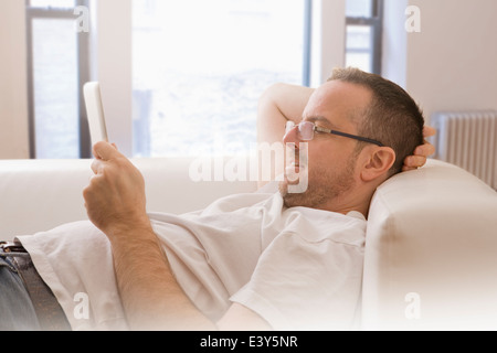 Uomo maturo sdraiata su un divano guardando a tavoletta digitale Foto Stock