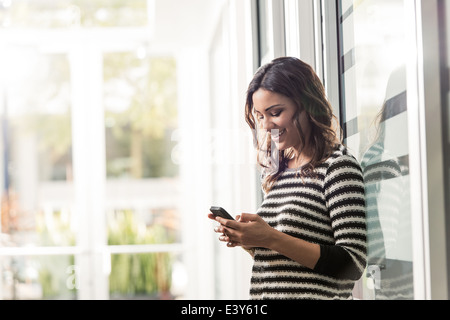 Giovane imprenditrice texting sullo smartphone in office Foto Stock