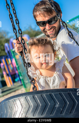 Padre e figlia toddler tirando una faccia su park swing Foto Stock