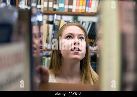 Giovane donna scegliendo libro in biblioteca Foto Stock