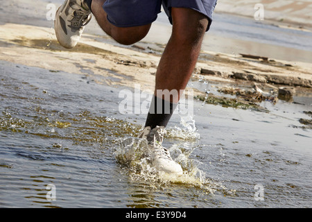 Vista ritagliata della giovane uomo che corre attraverso il fiume Foto Stock
