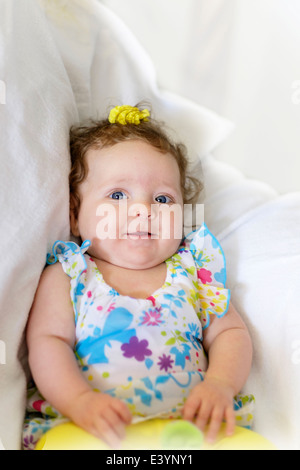 A tre mesi di età infantile caucasica ragazza sorridente e guardando la fotocamera. Seduta verso l'alto. Sfondo parzialmente riempito con il bianco. Foto Stock