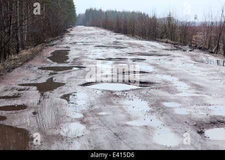 Rotture di strada asfaltata nel bosco con fori e pozzanghere, Russia Foto Stock