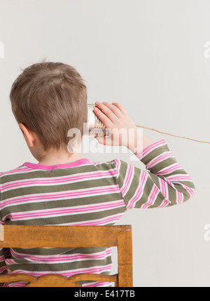 Bambino in ascolto con stagno possono telefonare a. Immagine concettuale dell'infanzia play e comunicazione. Foto Stock