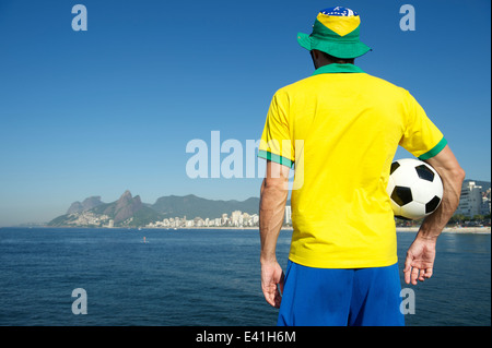 Uomo brasiliano nel team kit Brasile festeggia sulla tropicale sulla spiaggia di Ipanema di Rio de Janeiro Foto Stock