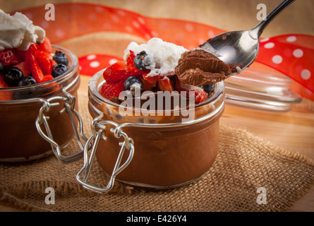 Mousse al cioccolato in contenitori di carino e rabboccato con mirtilli e fragole con panna montata. Chiudere con il cucchiaio. Vegane. Foto Stock