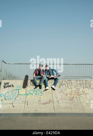 Giovani uomini in skatepark, utilizza lo smartphone Foto Stock