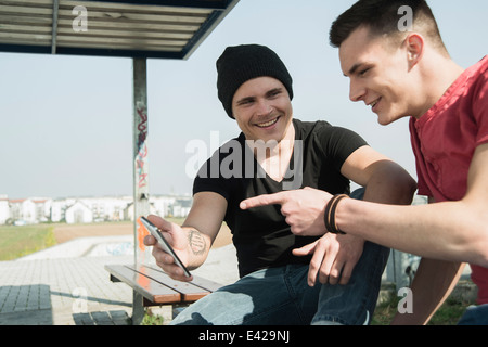 Giovani uomini in skatepark, utilizza lo smartphone Foto Stock